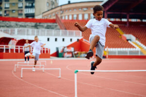 Little boy jumping over hurdles on running track