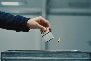 Hand releases a pack of cigarettes into a garbage can