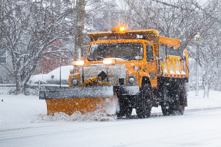 Yellow snowplow clearing a road during a snow storm