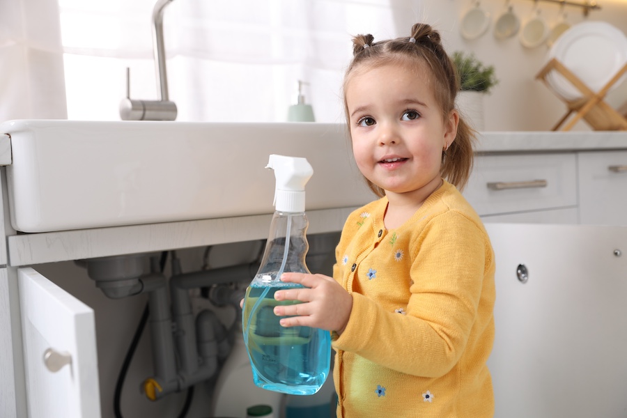 Little girl with bottle of cleaning product in kitchen