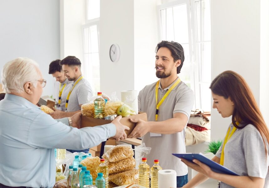 Poor people getting food aid at a charity center. Helpful volunteers give a senior man a box with pasta, oil, canned food and other stuff. Donation, poverty, help concept
