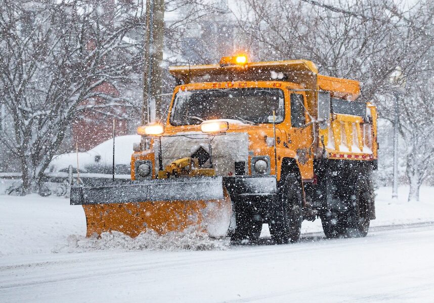Yellow snowplow clearing a road during a snow storm