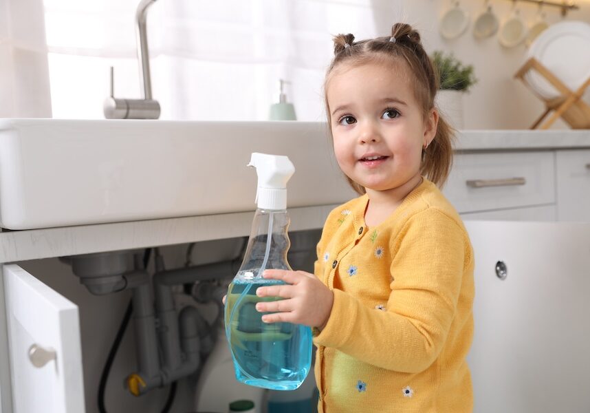 Little girl with bottle of cleaning product in kitchen