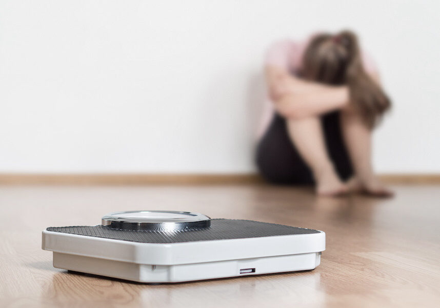 Weight loss fail concept. Scale and depressed, frustrated and sad woman sitting on floor holding head and arms on knees.