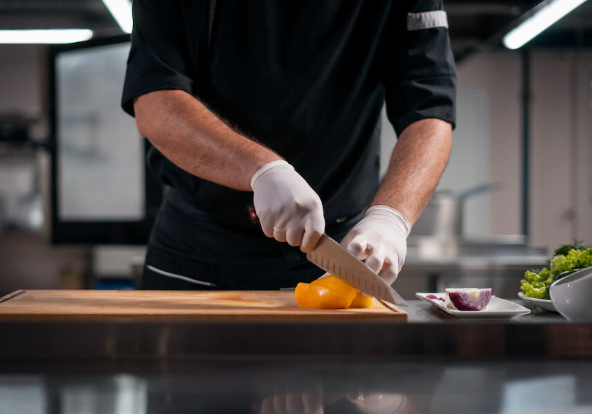 closeup of man gloved hands chop pepper for fresh salad at restaurant kitchen